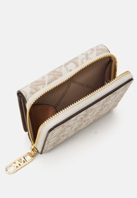Portefeuille crème avec fermeture éclair dorée, présentant un extérieur à motif, des accents en cuir marron et plusieurs compartiments pour cartes et billets.