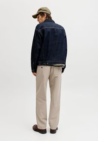 Σκούρο μπλε τζην μπουφάν, καπέλο χακί, μπεζ παντελόνια, καφέ παπούτσια. Το μπουφάν διαθέτει κλασικό σχέδιο με πλαϊνές τσέπες και ραφές λεπτομέρειες.