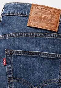 Poche de jean en denim bleu avec surpiqûres orange, étiquette rouge Levi's et étiquette en cuir marron Levi Strauss & Co. indiquant la taille W32 L32.