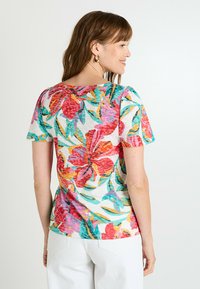 Camiseta de manga corta con estampado floral que presenta un colorido patrón de flores rosas y turquesas sobre un fondo blanco. Tejido suave y texturizado.