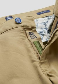 Beige Slim-Fit-Hose mit einem metallischen Knopf, Reißverschluss vorne und blauer Markenpatch; das Innenfutter weist ein gemustertes Design auf.