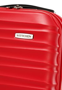 Rode hard-shell koffer met horizontale groeven, voorzien van een metalen logo plaat met het label "WITTCHEN" en een zwarte ritssluiting aan de bovenkant.