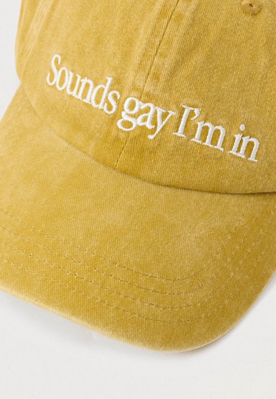 Žuta korduroy kapa s bijelim vezom teksta "Zvuci gay, idem." Ima strukturiranu visornu kapu i detalje šivanja.