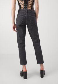 Black high-waisted jeans with a straight-leg cut. Features two back pockets and a leather patch on the waistband. Smooth denim texture.