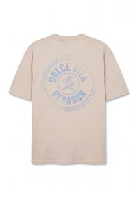 Μπεζ κοντομάνικο T-shirt με ξεθωριασμένο μπλε κυκλικό λογότυπο στην πλάτη, που απεικονίζει κεράσια και το κείμενο "Dolce Vita Pegador."