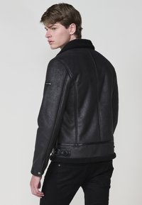 Giacca in pelle nera con colletto in shearling, finitura strutturata, tasca con zip laterale e un dettaglio in cintura in vita. Progettata per un look aderente.