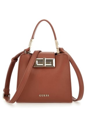 Brun Guess håndtaske i læder med topgreb, justerbar skulderrem og firkantet sølvspænde på hvid baggrund.