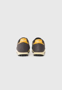Pantofi sport gri închis cu accente galbene și branding 'VEJA' pe călcâi, având un exterior texturat și o talpă contrastantă de nuanță crem.