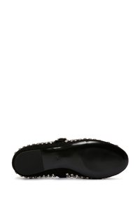 Zapato plano negro con una suela lisa, adornado con embellecedores redondos de plata alrededor de los bordes y una correa con hebilla en el lateral.