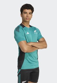 Teal rugbytröja med svarta detaljer, korta ärmar och svarta shorts. Har Adidas-logotyp och "ALL BLACK"-märke på bröstet.