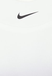 Bijela, rebrasta majica bez rukava s okruglim izrezom koja sadrži mali crni Nike logotip blizu ovratnika. Glatka tekstura, ležeran dizajn.