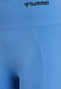 Blå idrottsshorts gjorda av ett mjukt, elastiskt tyg. Har ribbad textur, Hummel-logotyp och sömlös design för komfort.