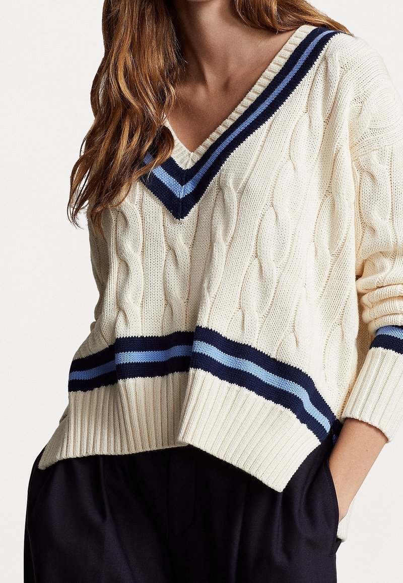 Krämfärgad kabelstickad tröja med V-ringning, med marinblå och ljusblå randiga detaljer vid halsringningen och fållen. Avslappnad passform, ribbade ärmslut.