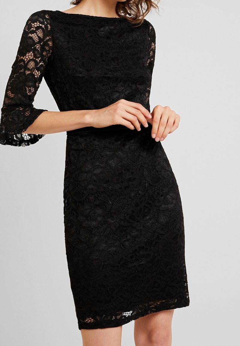 Svart spetsklänning med trekvartslånga ärmar, som har blommönster och en åtsittande design. Texturerad tyg med en vågig fåll.