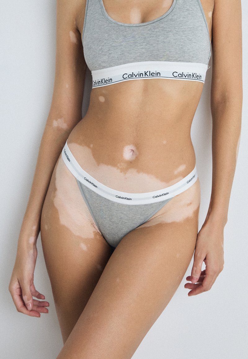Szara bawełniana braletka i stringi Calvin Klein z białym elastycznym paskiem z logo; gładka faktura, dopasowany krój i minimalne detale.