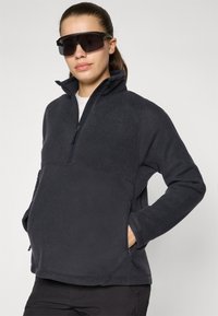 Must mustra pullover, millel pool-zip krae, külgmised taskud ja tavaline lõige. Pehme tekstuur ja minimaalne brändimine rinnal.