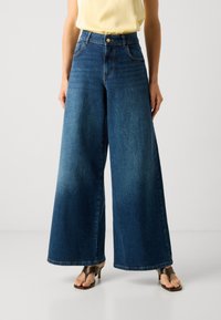 Jeans de corte largo em azul médio com uma cintura alta, apresentando um fecho de botão, bolsos laterais e um acabamento liso e texturizado.