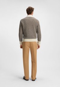 Suéter de punto marrón y crema con un patrón texturizado, puños y dobladillo acanalados; combinado con pantalones color canela y zapatos negros.