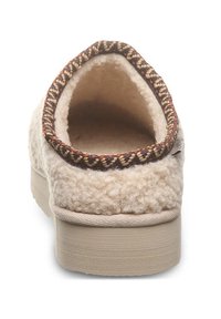 Cream-colored slipper with a textured wool upper, braided dark trim, and a flat light-colored sole. Open-back design for easy wear.