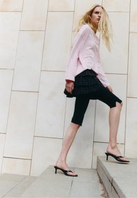 Mlada ženska z dolgimi rdečelaskimi lasmi, ki se vzpenja po kamnitih stopnicah, obdana v roza majico z dolgimi rokavi, večplastno krilo, črne pajkice in sandale z visokimi petami.