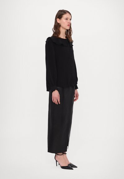 Black blouse with ruffled collar, long sleeves, and button closure, paired with a long black skirt and pointed black heels.