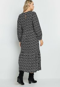 Largo vestido negro con lunares blancos, escote redondeado, mangas largas y falda en capas. Presenta una pequeña abertura en forma de gota en la parte posterior. Estilizado con botas negras.