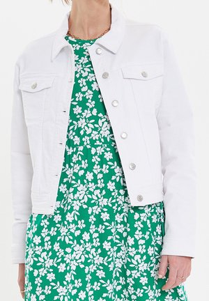 Hvid denimjakke med sølvknapper båret over en grøn blomsterkjole med hvide blomster og små blade på stoffet.