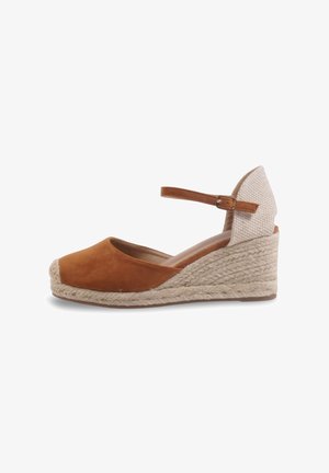 Espadrille compensée en daim marron avec talon tissé beige, boucle à la bride de cheville et bout fermé sur fond blanc.