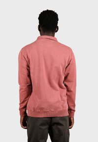 Pull-over à manches longues en coton couleur rose corail, avec un col et des poignets côtelés, une texture lisse et un design minimaliste.