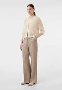 Beige, offenes Strickcardigan über einem hellen Top, kombiniert mit lockeren beigen Hosen und neutralen Sandalen. Einfaches, atmungsaktives Design mit Knöpfen.