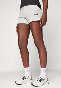 Harmaat puuvillaiset urheilushortsit, joissa on musta Puma-logo, yhdistetty valkoisiin urheilukenkiin ja valkoisiin sukkiin. Shortseissa on tiukka malli.