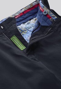 Pantalon noir avec fermeture éclair, doté d'une doublure à motif bleu et d'une étiquette verte indiquant des matériaux écologiques.