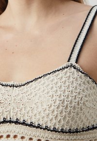 Top in maglia color crema con un motivo testurizzato e bordo nero lungo il colletto e le bretelle, caratterizzato da un design in pizzo e punti aperti.