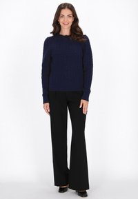 Marineblauer Kabelstrickpullover mit langen Ärmeln und gerippten Bündchen, kombiniert mit schwarzen ausgestellten Hosen und High Heels. Sauberes, strukturiertes Stoffdesign.