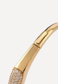Złoty oprawa okularów przeciwsłonecznych z teksturowanym obszarem ozdobionym przezroczystymi cyrkoniami, smukły design i zaokrąglony kształt. Gładkie, błyszczące wykończenie.