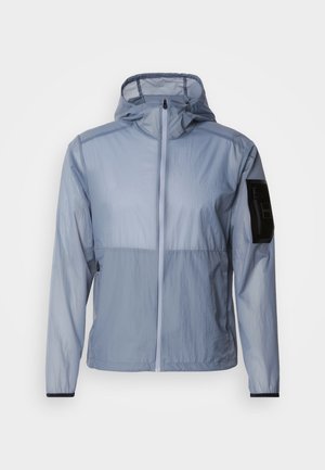 Jacket leveira de cor azul clara, leve, com fecho completa, capuz ajustável e bolso preto na manga esquerda. Textura suave e design minimalista.