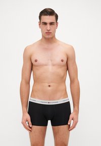 Fekete boxer alsónadrág szürke derékrésszel, amelyen a "TOMMY HILFIGER" logó szerepel. Az anyag simának tűnik, a testhez simuló dizájn kiemeli a testalkatot.