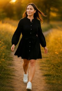 Abito nero con bottoni, vita con cintura, maniche lunghe e gonna a ruota, abbinato a sneakers bianche, ambientato su un sentiero erboso.