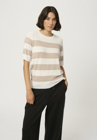 Bež in bela črtasta pletena majica s kratkimi rokavi in okroglim izrezom, kombinirana s črnimi hlačami. Mehka tekstura, sproščen kroj.