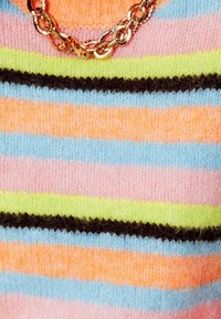 Pull tricoté multicolore avec des rayures horizontales rose, orange, bleu, vert et marron. Détail en chaîne dorée au niveau de l'encolure.
