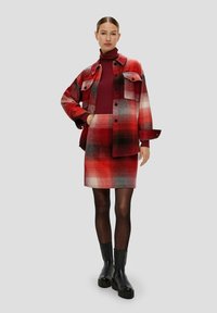 Rot-schwarz kariertes übergroßes Hemd-Jacke, kombiniert mit einem passenden Bleistiftrock. Verfügt über lange Ärmel, Taschen und strukturierten Stoff. Schwarze Stiefeletten.