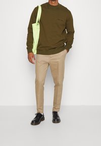 Sudadera verde oliva con cuello redondo, pantalones beiges, zapatos negros y una bolsa tote verde claro. Diseño simple sin patrones visibles.