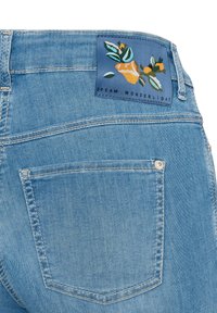 Hellblaue Jeans aus Denim mit einem floralen Etikett auf dem Bund, das "DREAM WONDERLIGHT" liest; verfügt über eine einzelne Gesäßtasche.