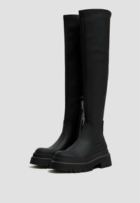 Bottes noires montant jusqu'aux genoux avec une finition en cuir lisse, dotées d'une semelle épaisse et d'une fermeture éclair latérale pour un enfilage facile.