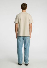 Short-sleeve beige t-shirt with a straight cut, paired with light wash denim jeans. The fabric appears soft and smooth.