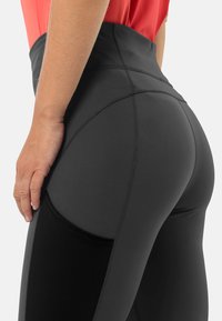 Zwarte high-waisted leggings hebben een gladde textuur, contrasterende stiksels en een zijzak met een zwarte inzet voor extra functionaliteit.