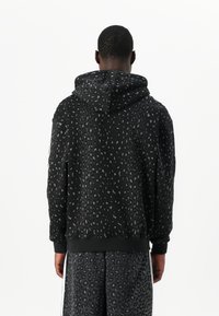 Svart hoodie med grå leopardmönster, mjukt material, justerbar huva, ribbade muddar och fåll. Matchas med shorts i samma mönster.