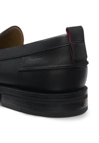 Zwarte lederen schoen met een ronde neus en een rubberen zool met textuur. Opvallend rood accent op de hiel en stikseldetail op het bovendeel.