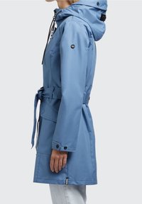 Blå vattentät jacka med huva, justerbart bälte, tryckknappar och slät textur. Har sidofickor och logodetalj på ärmen.