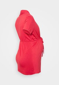 Vestido de maternidade vermelho em tecido suave e elástico. Mangas curtas, detalhe de cintura amarrada e design de barra curva com um corte relaxado.